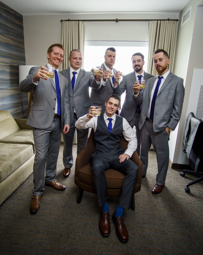 Groom and groomsmen from a wedding party holding drink glasses up in a cheers salute