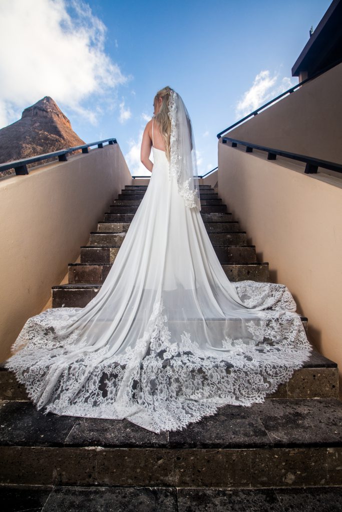 Woman wearing a long white wedding dress standing at the top of a stone staircase